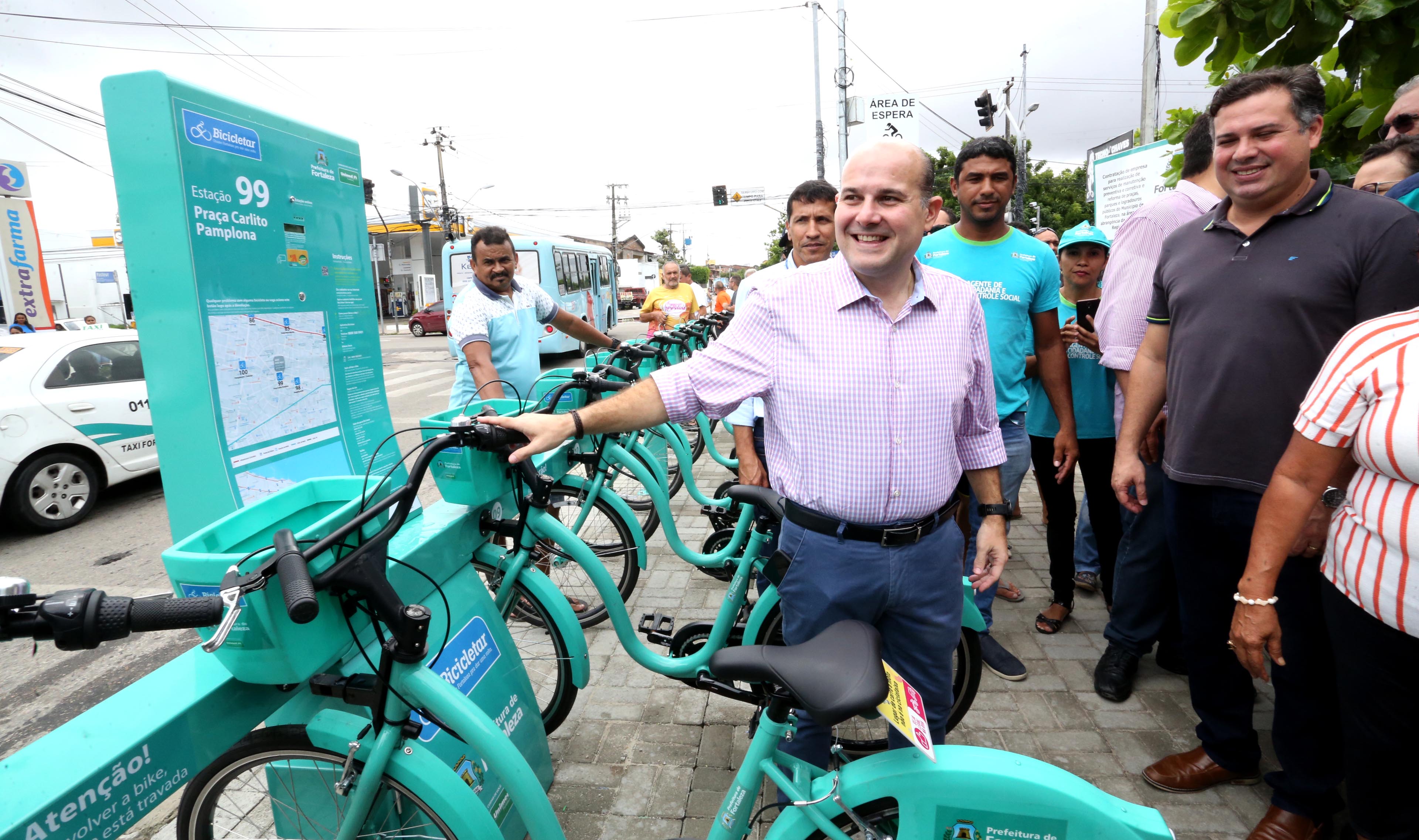 prefeito em pé sorrindo ao lado de bicicletas e pessoas ao fundo